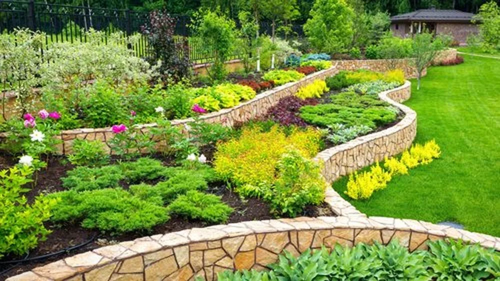 Curved stone-bordered garden beds filled with shrubs, flowers, and green plants